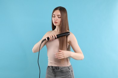 Photo of Woman straightening her beautiful hair on light blue background