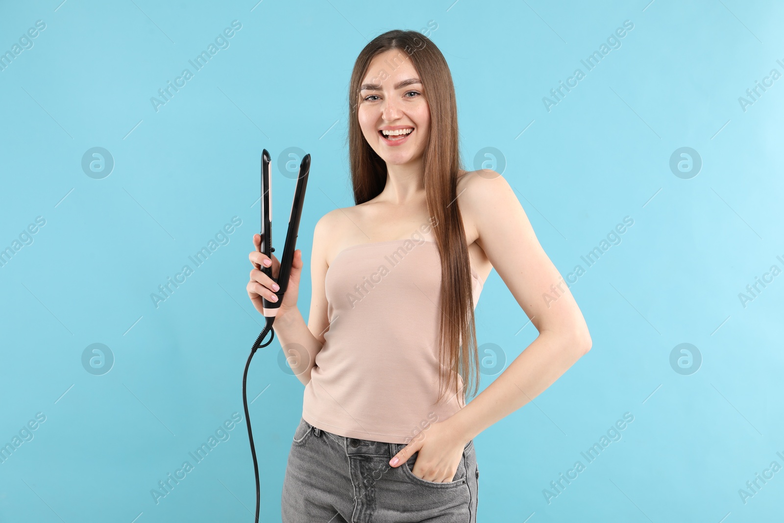 Woman with beautiful hair and straightener on light blue background Photo of Woman with beautiful hair and straightener on light blue background