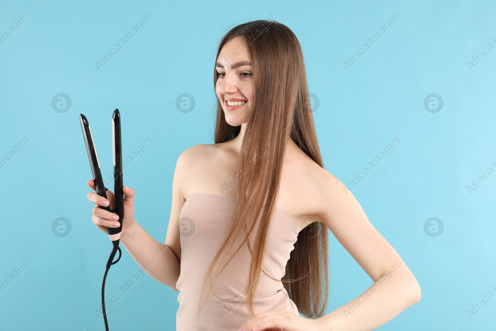 Woman with beautiful hair and straightener on light blue background Photo of Woman with beautiful hair and straightener on light blue background