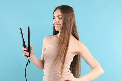 Photo of Woman with beautiful hair and straightener on light blue background