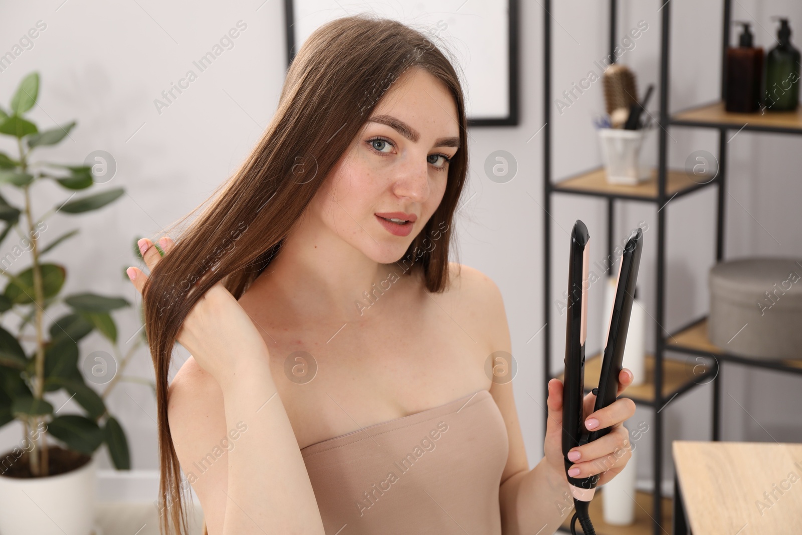 Woman with beautiful hair and straightener indoors Photo of Woman with beautiful hair and straightener indoors