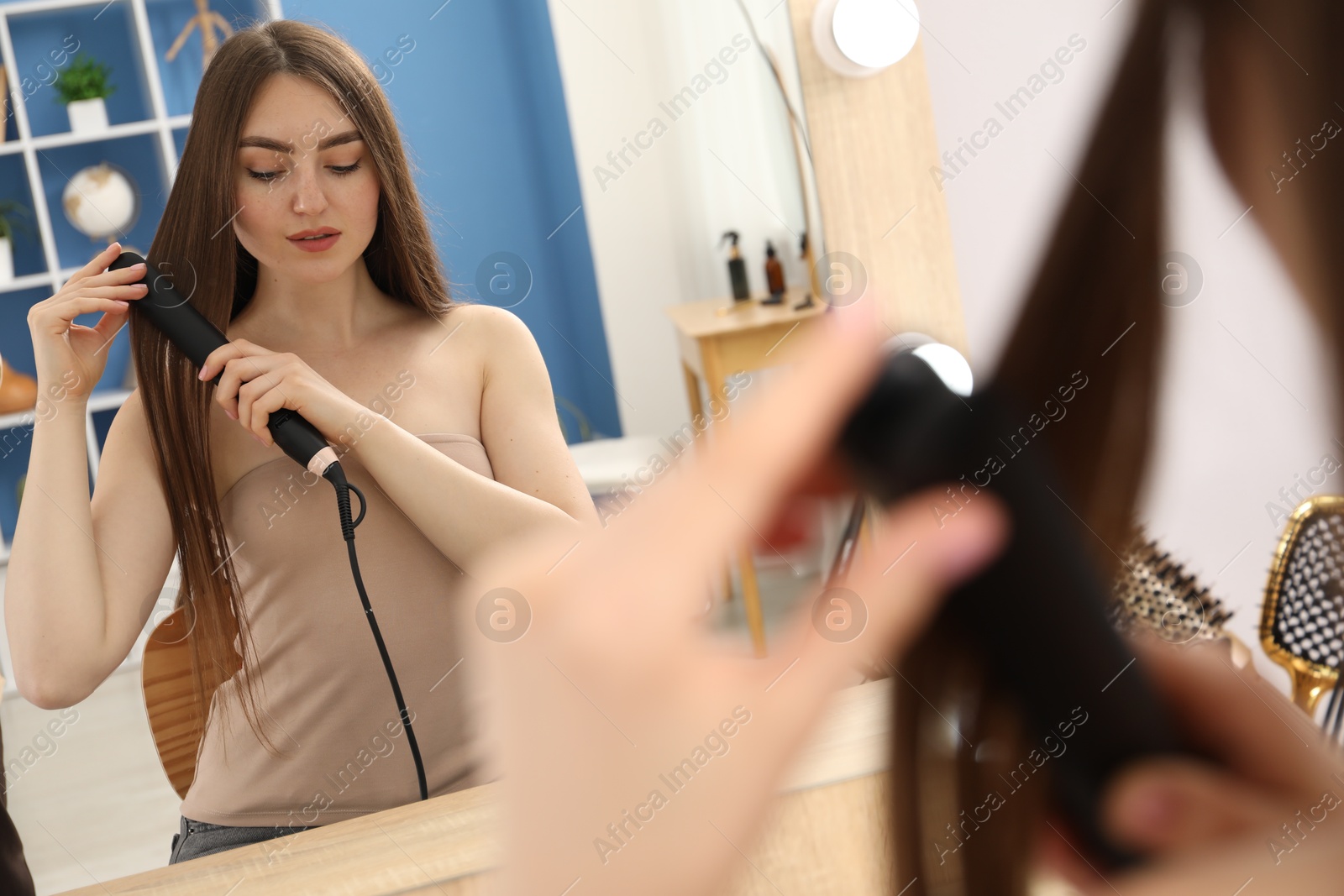 Woman straightening her hair near mirror indoors, closeup Photo of Woman straightening her hair near mirror indoors, closeup