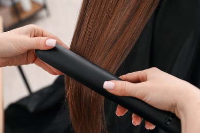 Photo of Hairdresser straightening woman's hair in salon, closeup