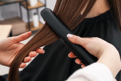 Photo of Hairdresser straightening woman's hair in salon, closeup