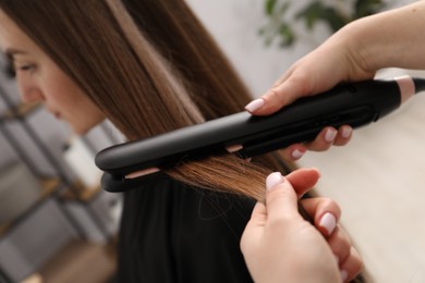 Photo of Hairdresser straightening woman's hair in salon, closeup