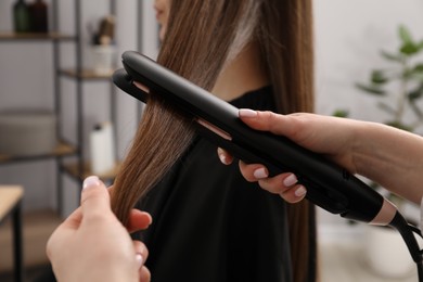 Photo of Hairdresser straightening woman's hair in salon, closeup