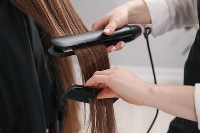 Photo of Hairdresser straightening woman's hair in salon, closeup