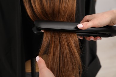 Photo of Hairdresser straightening woman's hair in salon, closeup