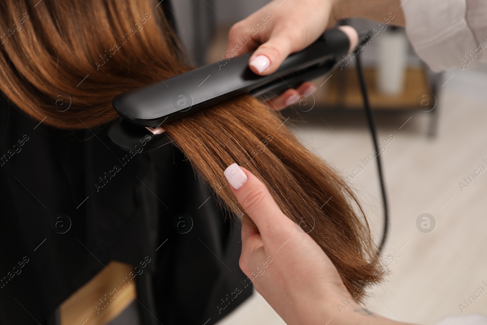 Hairdresser straightening woman's hair in salon, closeup Photo of Hairdresser straightening woman's hair in salon, closeup