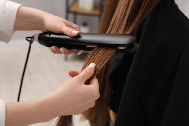 Photo of Hairdresser straightening woman's hair in salon, closeup