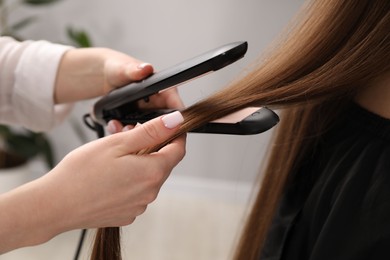 Photo of Hairdresser straightening woman's hair in salon, closeup