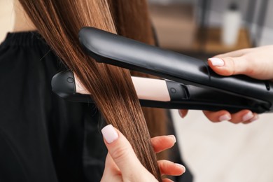 Photo of Hairdresser straightening woman's hair in salon, closeup