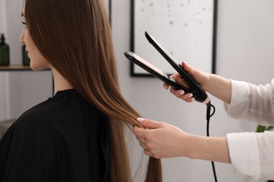 Photo of Hairdresser straightening woman's hair in salon, closeup