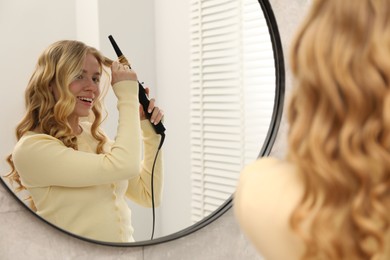Photo of Woman curling her hair near mirror indoors