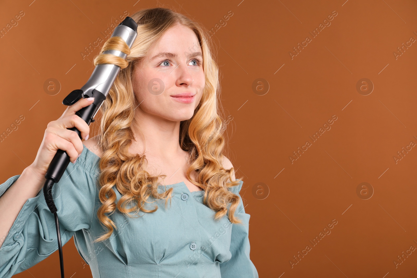 Woman curling her hair on brown background. Space for text Photo of Woman curling her hair on brown background. Space for text