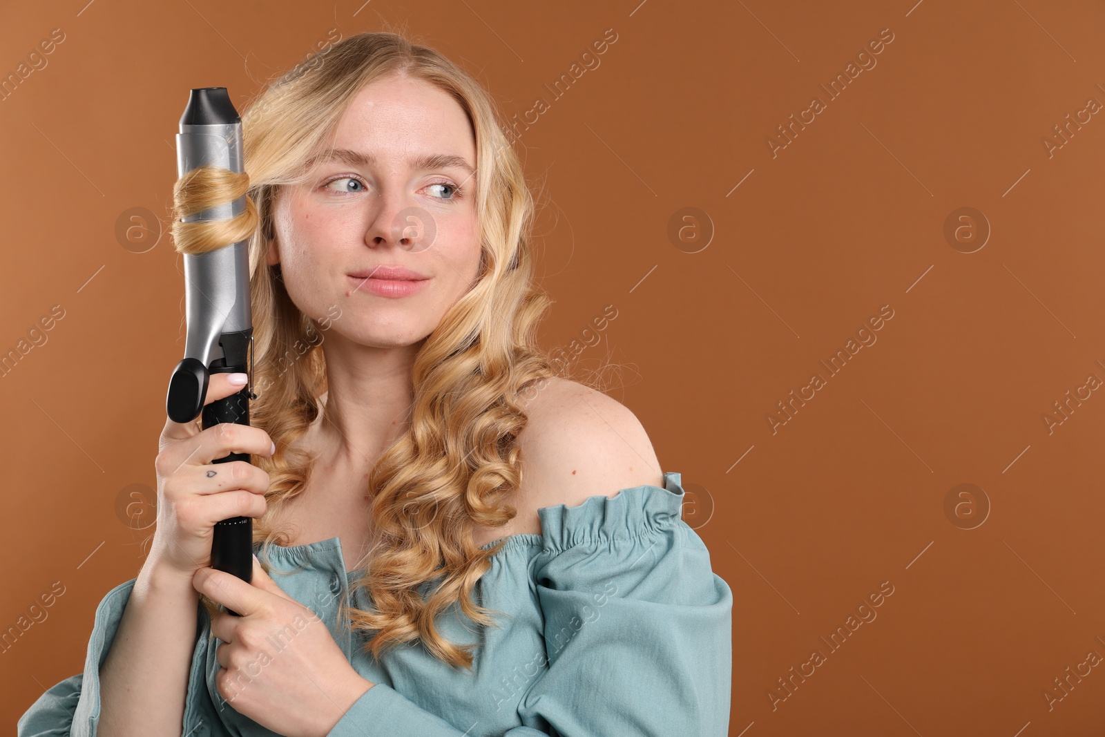 Woman curling her hair on brown background. Space for text Photo of Woman curling her hair on brown background. Space for text