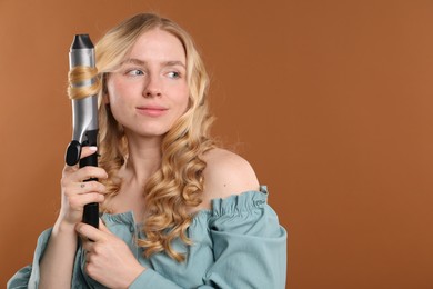 Photo of Woman curling her hair on brown background. Space for text