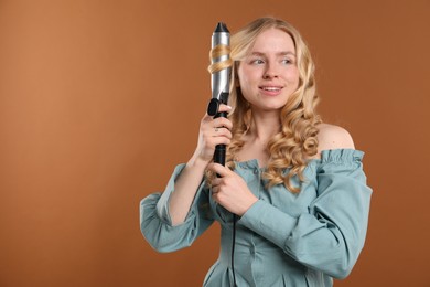 Photo of Woman curling her hair on brown background. Space for text