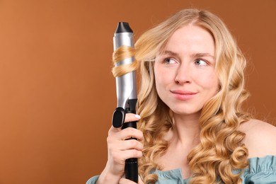 Photo of Woman curling her hair on brown background. Space for text