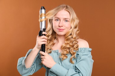 Photo of Woman curling her hair on brown background