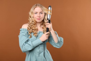 Photo of Woman curling her hair on brown background