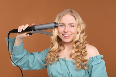 Photo of Woman with beautiful hair and curling iron on brown background