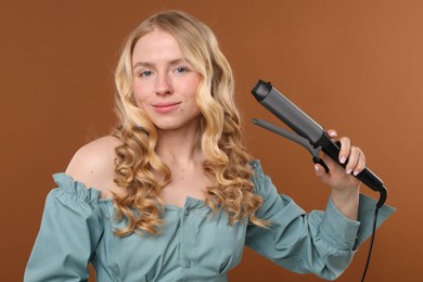 Photo of Woman with beautiful hair and curling iron on brown background