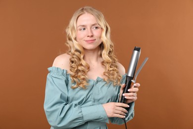 Photo of Woman with beautiful hair and curling iron on brown background