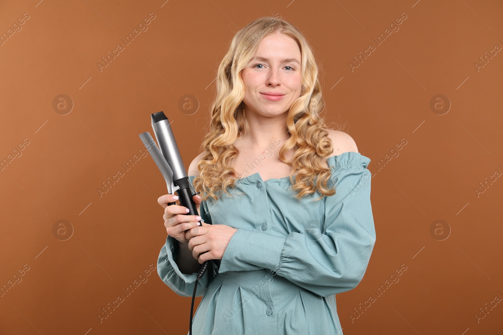Woman with beautiful hair and curling iron on brown background Photo of Woman with beautiful hair and curling iron on brown background