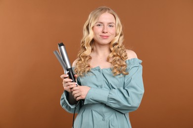 Photo of Woman with beautiful hair and curling iron on brown background