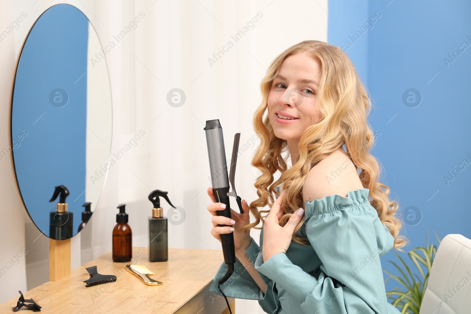 Woman styling her hair with curling iron indoors Photo of Woman styling her hair with curling iron indoors