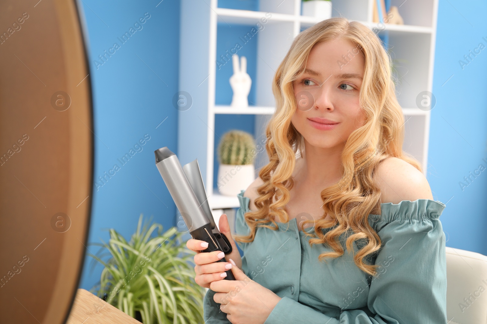 Woman styling her hair with curling iron indoors Photo of Woman styling her hair with curling iron indoors