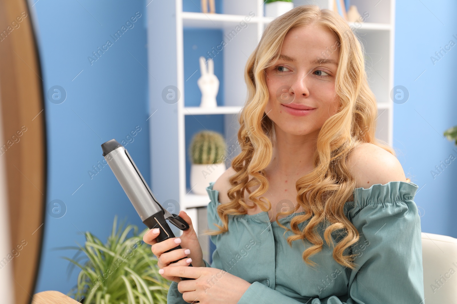 Woman styling her hair with curling iron indoors Photo of Woman styling her hair with curling iron indoors