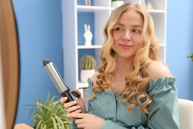 Photo of Woman styling her hair with curling iron indoors