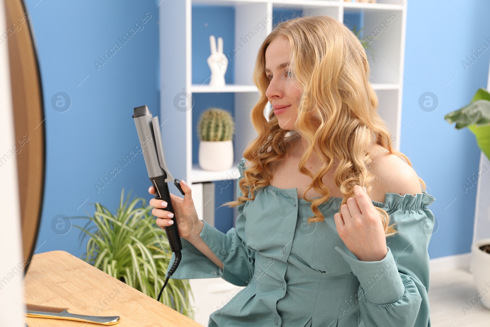 Woman styling her hair with curling iron indoors Photo of Woman styling her hair with curling iron indoors