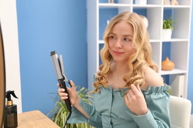 Photo of Woman styling her hair with curling iron indoors