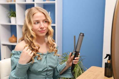 Photo of Woman styling her hair with curling iron indoors