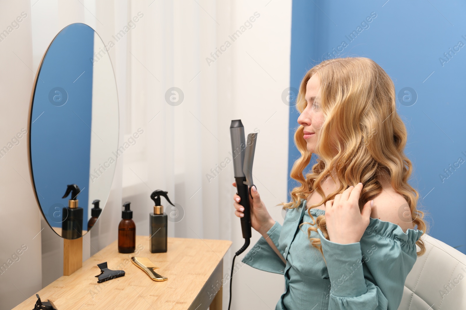 Woman styling her hair with curling iron indoors Photo of Woman styling her hair with curling iron indoors