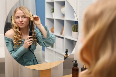 Photo of Woman curling her hair near mirror indoors