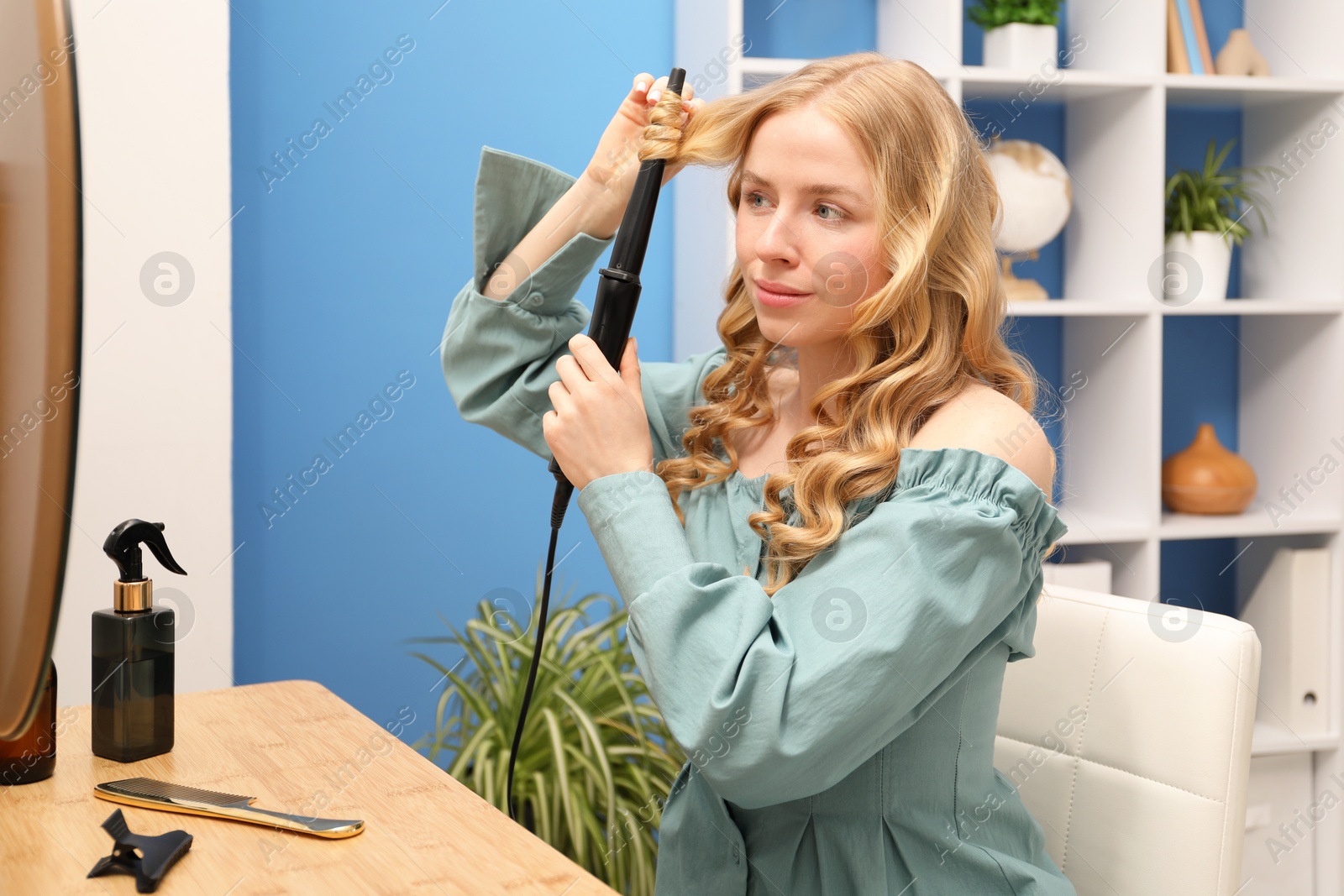 Woman styling her hair with curling iron indoors Photo of Woman styling her hair with curling iron indoors