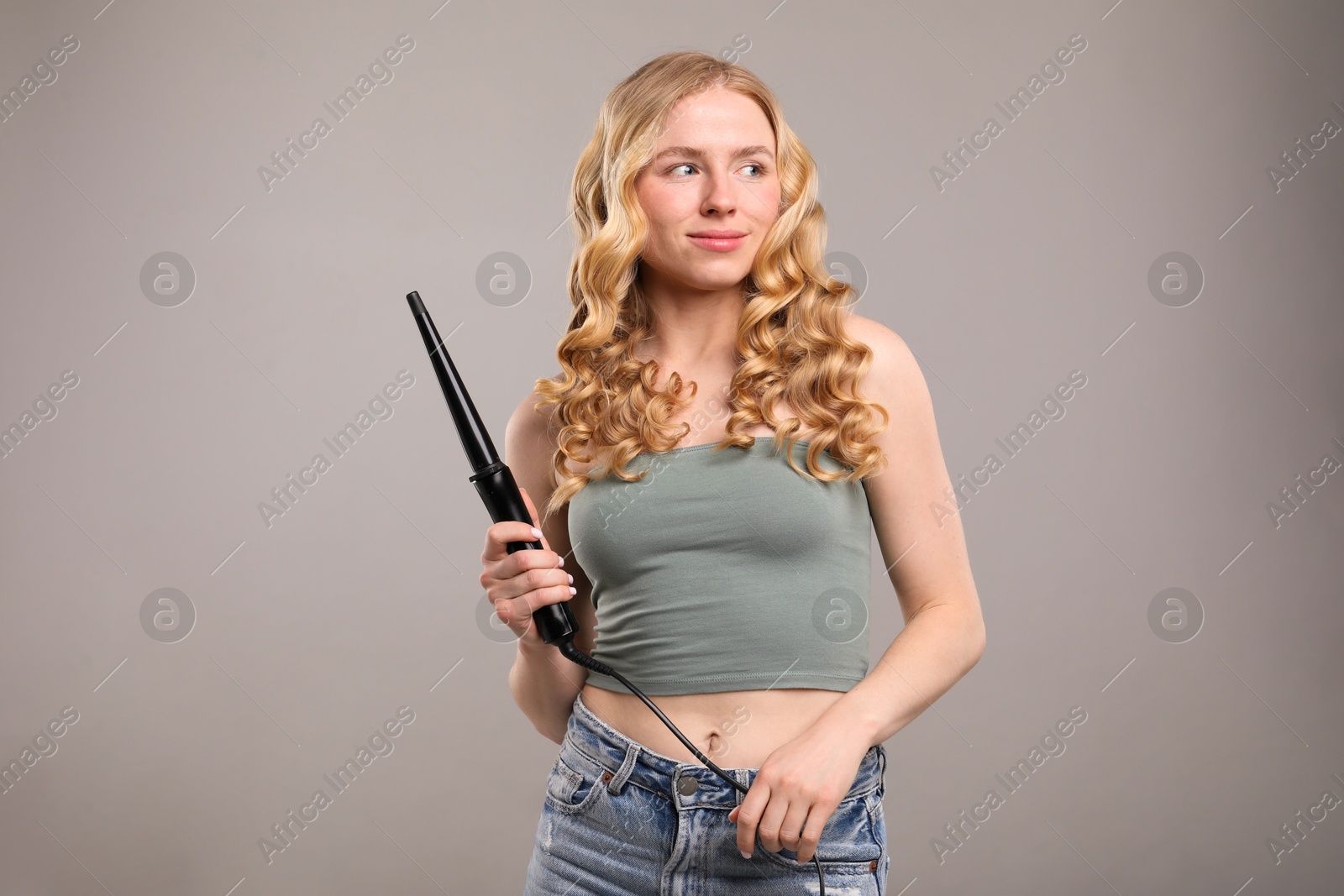 Woman with beautiful hair and curling iron on grey background Photo of Woman with beautiful hair and curling iron on grey background