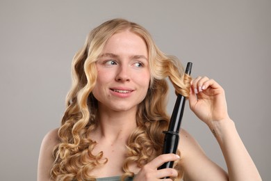 Photo of Woman curling her hair on grey background
