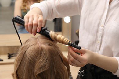 Photo of Hairdresser curling woman's hair in salon, closeup