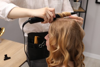 Photo of Hairdresser curling woman's hair in salon, closeup