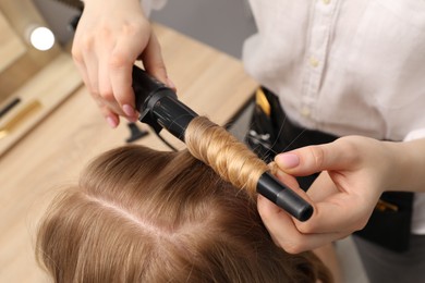 Photo of Hairdresser curling woman's hair in salon, closeup