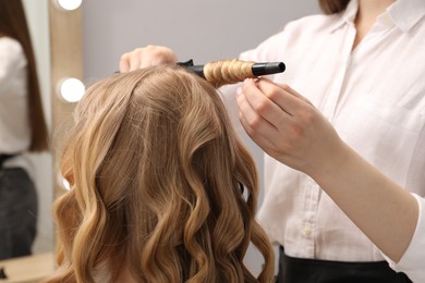 Photo of Hairdresser curling woman's hair in salon, closeup