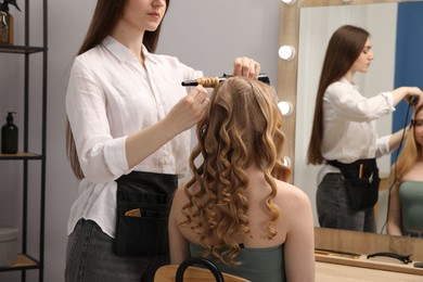 Photo of Hairdresser curling woman's hair in salon, closeup