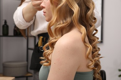 Photo of Hairdresser curling woman's hair in salon, closeup