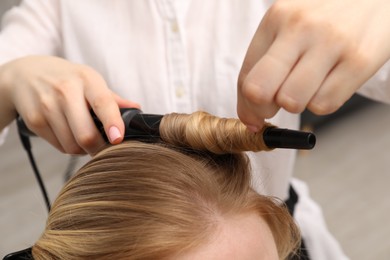 Photo of Hairdresser curling woman's hair in salon, closeup