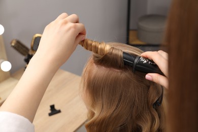 Photo of Hairdresser curling woman's hair in salon, closeup